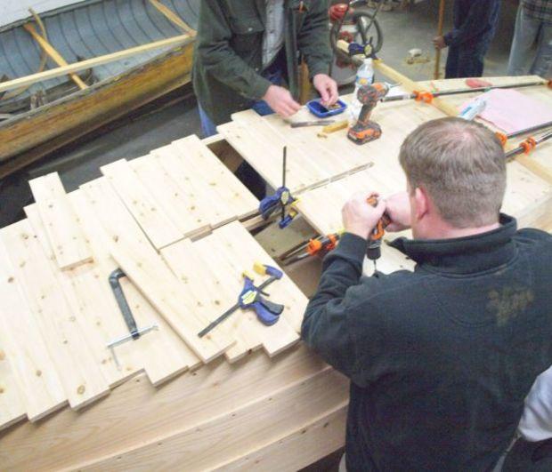 Two students fit bottom planking around the centerboard trunk for the school’s Pretty Good Skiff project.