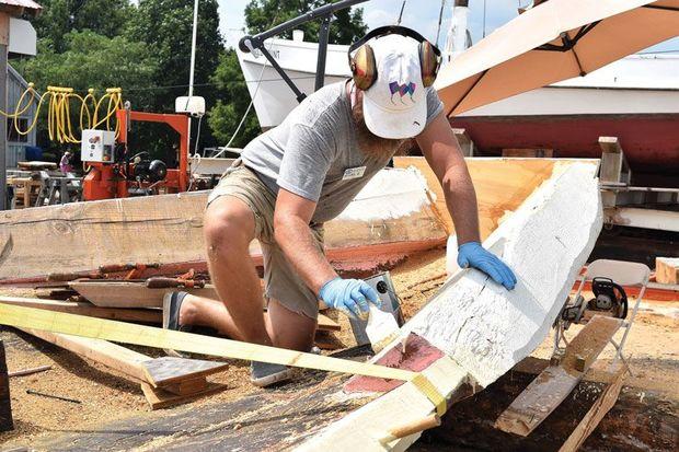 Chesapeake Bay Maritime Museum boatyard manager Michael Gorman applies paint to a chunk on the new nine-log hull for Edna E. Lockwood.